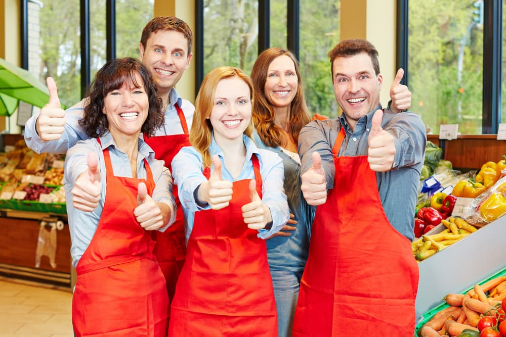 Equipe de funcionários feliz em um supermercado segurando seus polegares para cima.