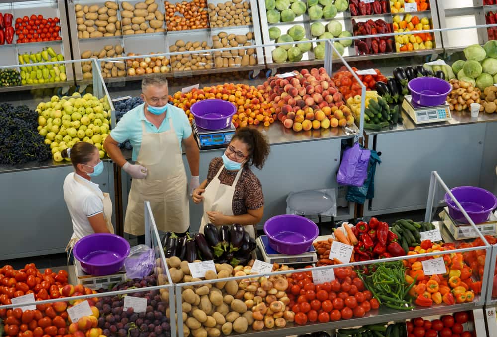 Três pessoas em uma feira de frutas e legumes.